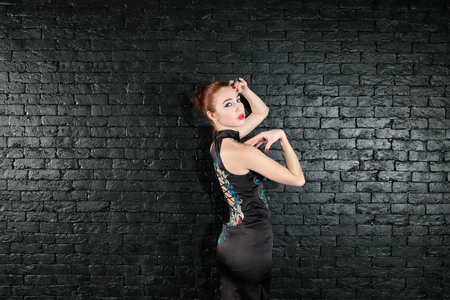 Beautiful young woman in black dress with makeup poses in studio near black wallの写真素材