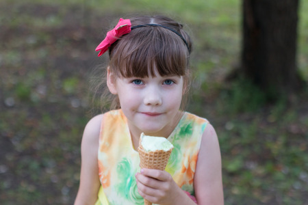 Beautiful little girl in a coloured sundress eating ice cream on a warm summer dayの写真素材