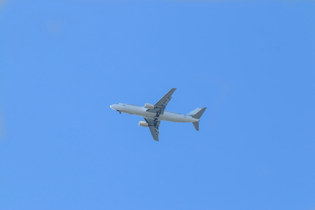 White passenger plane flies highly in the sky on a bright Sunny day without cloudsの写真素材