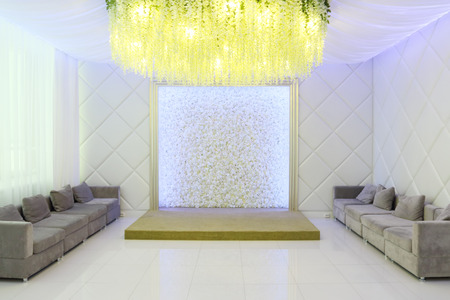 Flowers hanging from ceiling, wall with white roses, stage, couches in hall for weddingのeditorial素材