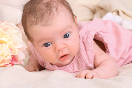 Sweet little baby quietly lying on the bed with a white blanket and looks with curiosityの写真素材