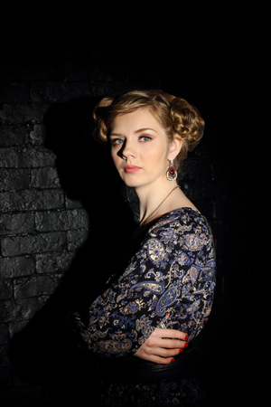 Beautiful young woman with hairdo and makeup poses in dark studioの写真素材