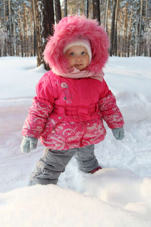 Little girl in pink stands in forest and smiles in winter sunny dayの写真素材