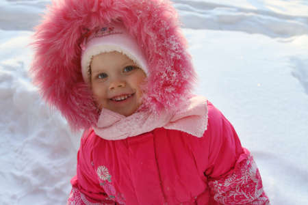 Little girl in pink stands and smiles in winter sunny day outdoorの写真素材