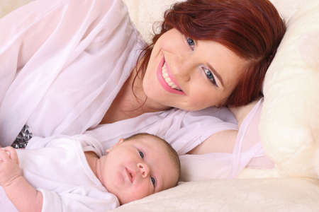 Beautiful young mother lying on the bed with his tiny child and glows with happinessの写真素材