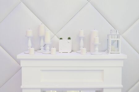White decorative fireplace, candles, clock, lantern, white wallsの写真素材