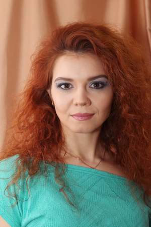 Beautiful young woman with curly hair and makeup poses near curtain, closeupの写真素材