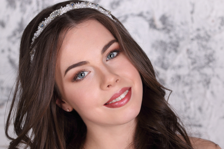 Beautiful brunette in diadem and with hairdo smiles in studio, close-upの写真素材