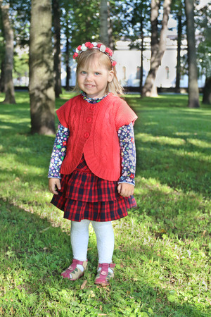 Happy little girl in red smiles in summer green park at sunny dayの写真素材