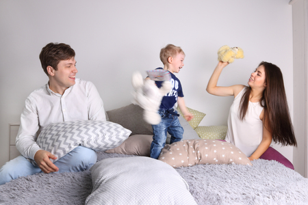 Young father, mother, little cute son play on bed among pillows at homeの写真素材