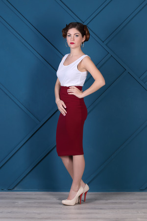 Beautiful woman with hairdo and in skirt poses in blue studioの写真素材