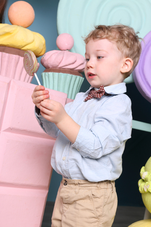 Little funny boy holds lollipop in studio with big fake sweetsの写真素材