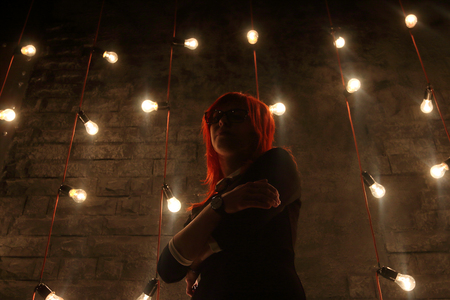 Girl in glasses poses near wall in black studio with garlands of lamps, under view