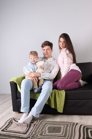 Young father, mother, little son sit on couch with toy bear in roomの写真素材