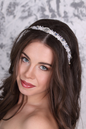 Pretty brunette in diadem and with hairdo smiles in studio, close-upの写真素材