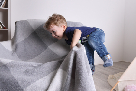 Happy little cute boy play on armchair in living room at homeの写真素材