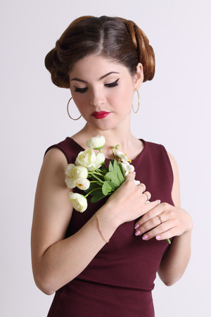Beautiful woman with hairdo and earrings holds flowers in grey studioの写真素材