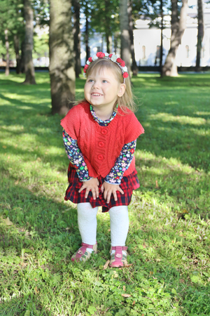 Happy little girl in red stands in summer green park at sunny dayの写真素材