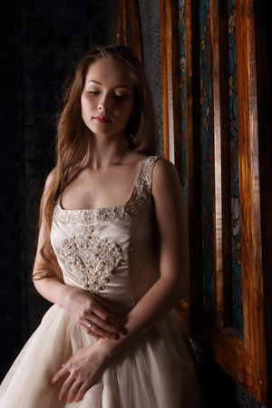 Pretty young woman in long dress dreams near window in black studioの写真素材