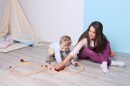 Young happy mother and little son play with wooden railway on floorの写真素材