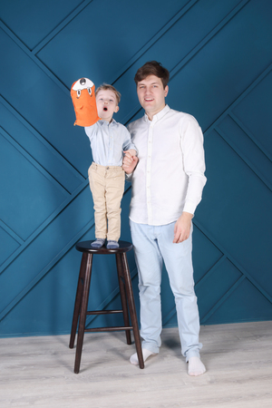 Young handsome man and little son on stool pose in blue studioの写真素材