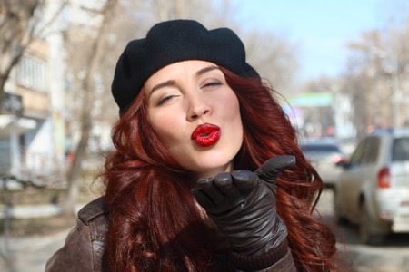 Young woman in leather gloves and beret sends air kiss on street at sunny spring dayの写真素材