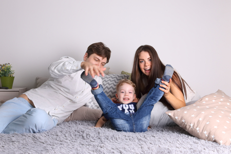 Handsome father, mother, little cute son play on bed among pillows in roomの写真素材