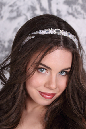 Beautiful brunette in diadem and with hairdo poses in studio, close-upの写真素材