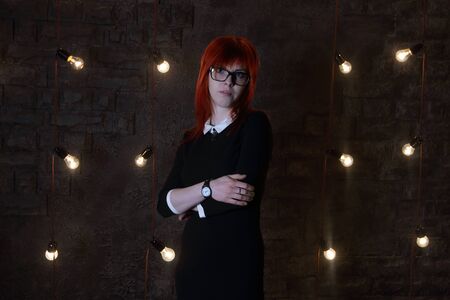 Girl with wristwatch poses near wall in black studio with garlands of lampsの写真素材