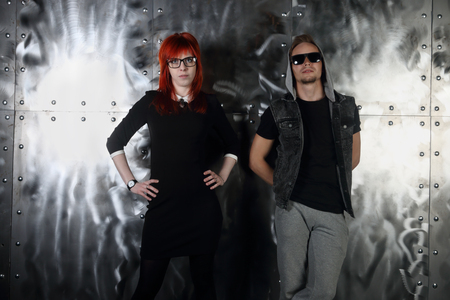 Pretty red hair girl and young man pose together near metal wall in studioの写真素材