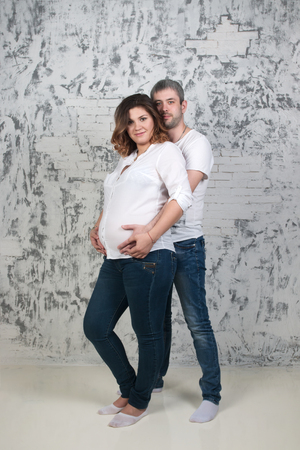 Young pretty pregnant woman and man in jeans poses in white studioの写真素材