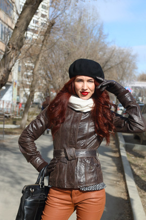 Young woman in leather jacket and gloves stands on street at sunny spring dayの写真素材