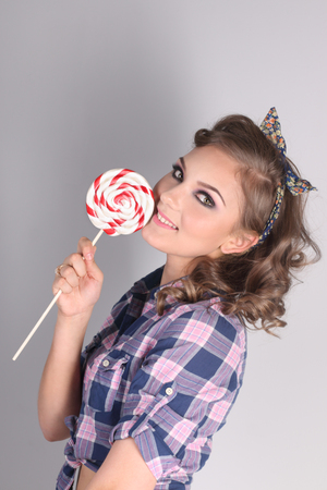 Pinup beautiful girl in checkered shirt poses with lollipop in studioの写真素材
