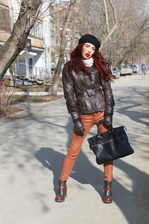 Girl in leather jacket and gloves stands on street at sunny spring dayの写真素材