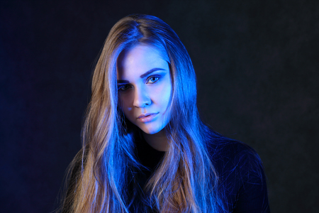Pretty blonde with long hair in black poses in black studio with blue lightの写真素材