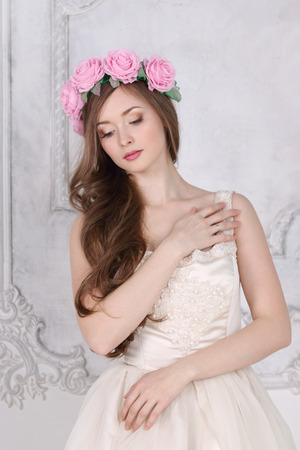 Beautiful woman in roses wreath with long hair poses in white studioの写真素材
