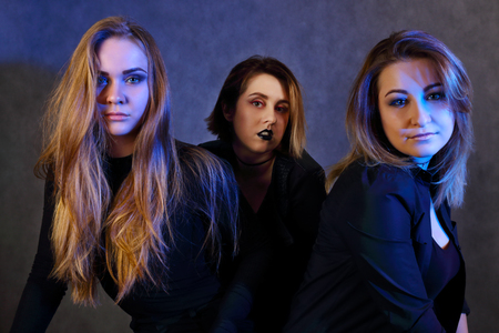 Three young girls with make up in black clothes sit in studio with blue lightの写真素材