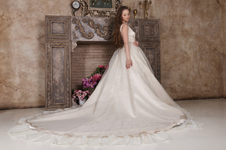 Young woman in long dress poses near fake fireplace in studioの写真素材