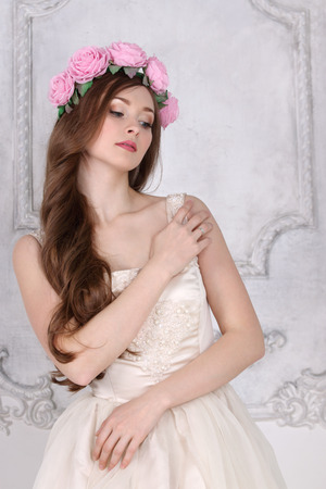 Beautiful young woman in roses wreath with long hair poses in white studioの写真素材
