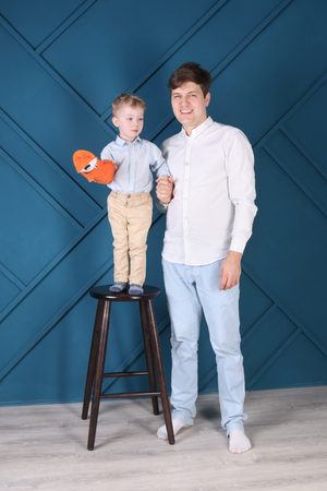 Young handsome father and little son on stool pose in blue studioの写真素材