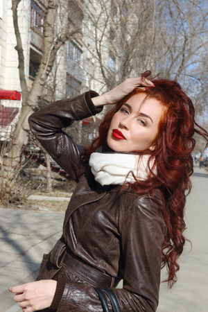 Girl with red hair in leather jacket poses outdoor at sunny spring dayの写真素材