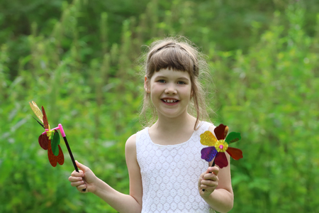 Little pretty girl with two windmills toys in summer green forestの写真素材