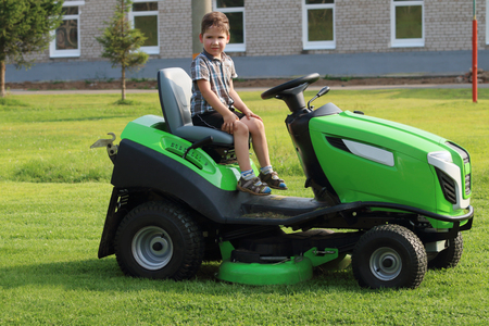 Little boy sits on lawn on green grass near building at summer dayの写真素材