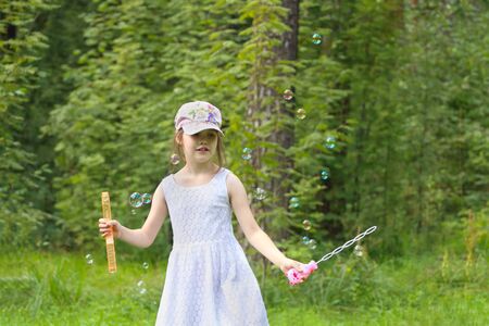 Happy girl in cap plays with soap bubbles in summer green parkの写真素材