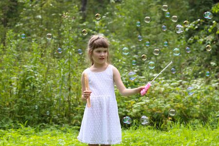 Pretty girl in white dress plays with soap bubbles in summer green forestの写真素材