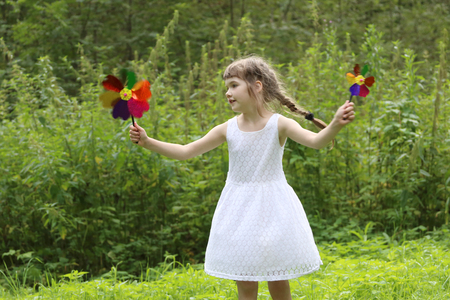 Pretty little girl with two windmills spins in summer green forestの写真素材