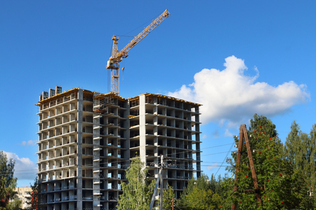 Concrete residential building frame under construction and crane at sunny day among treesの写真素材