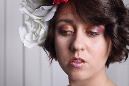 young brunette woman with clean skin, make-up and flower wreath in her hair posing at white door, closeup, looks downの写真素材