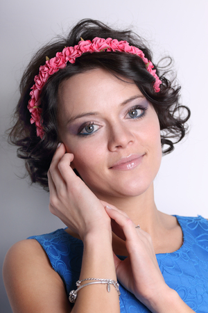 Beautiful young brunette woman with wreath on her head and make-up on grey background, touching her cheekの写真素材