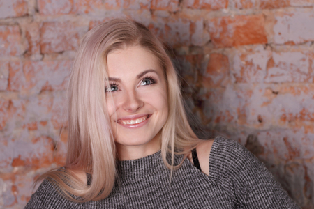 portrait of beautiful smiling blonde woman in striped blouse posing near brick wall, looks upの写真素材